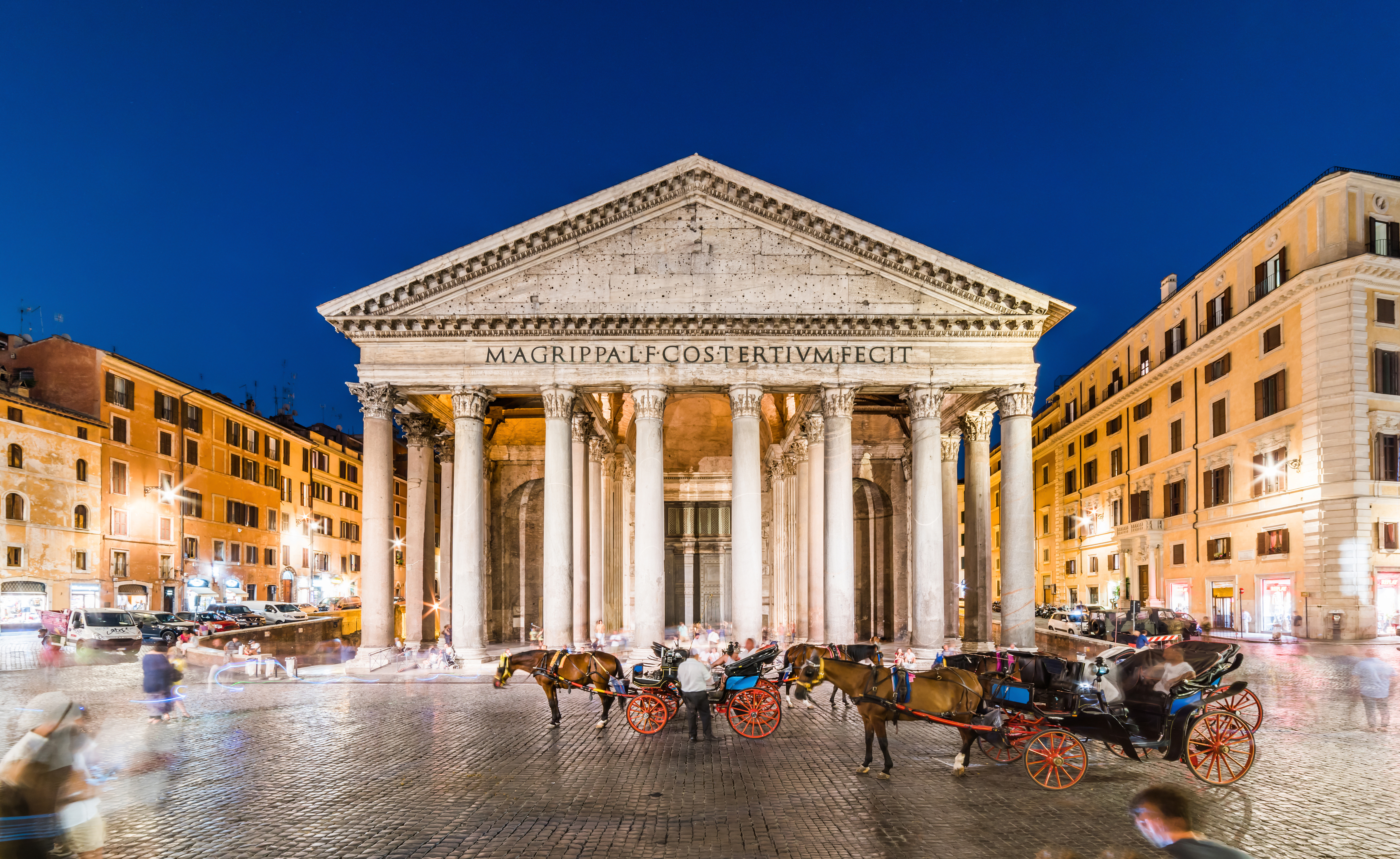 Horse-drawn carriages wait outside an ancient temple building in Rome