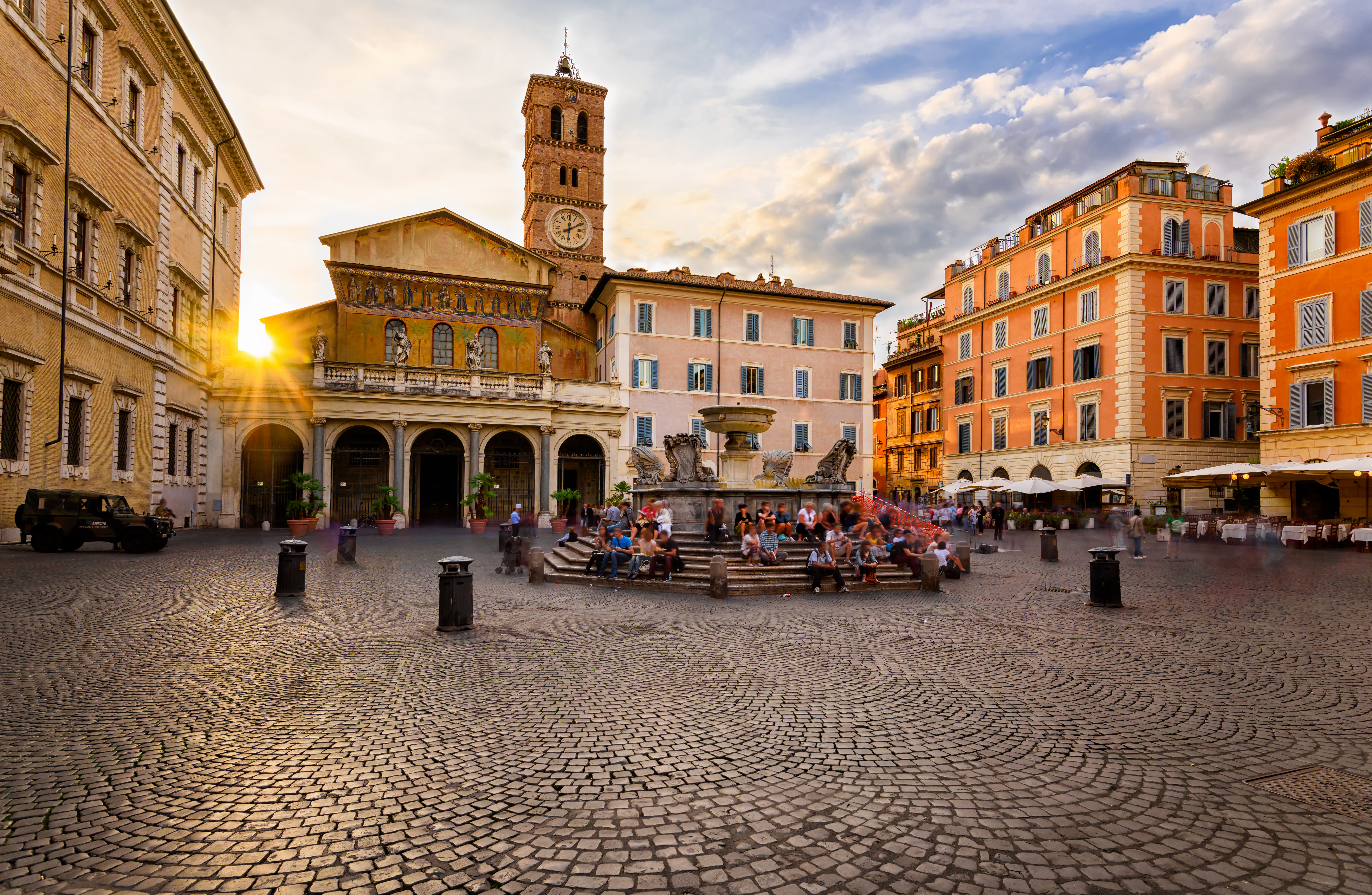 A city square with a church in the corner. The sun sets behind the church