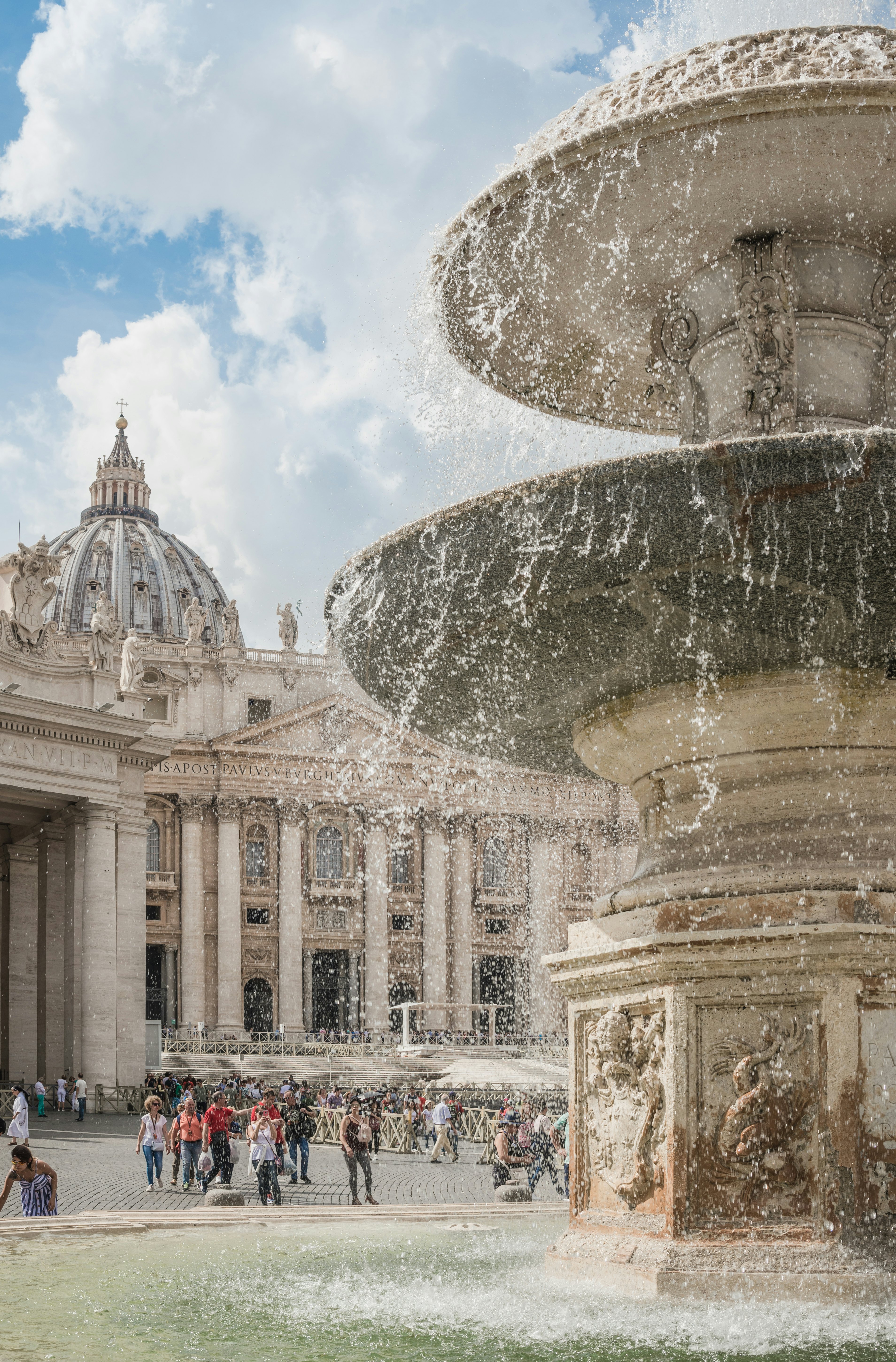 People gather in front of a marble fountain on a plaza
