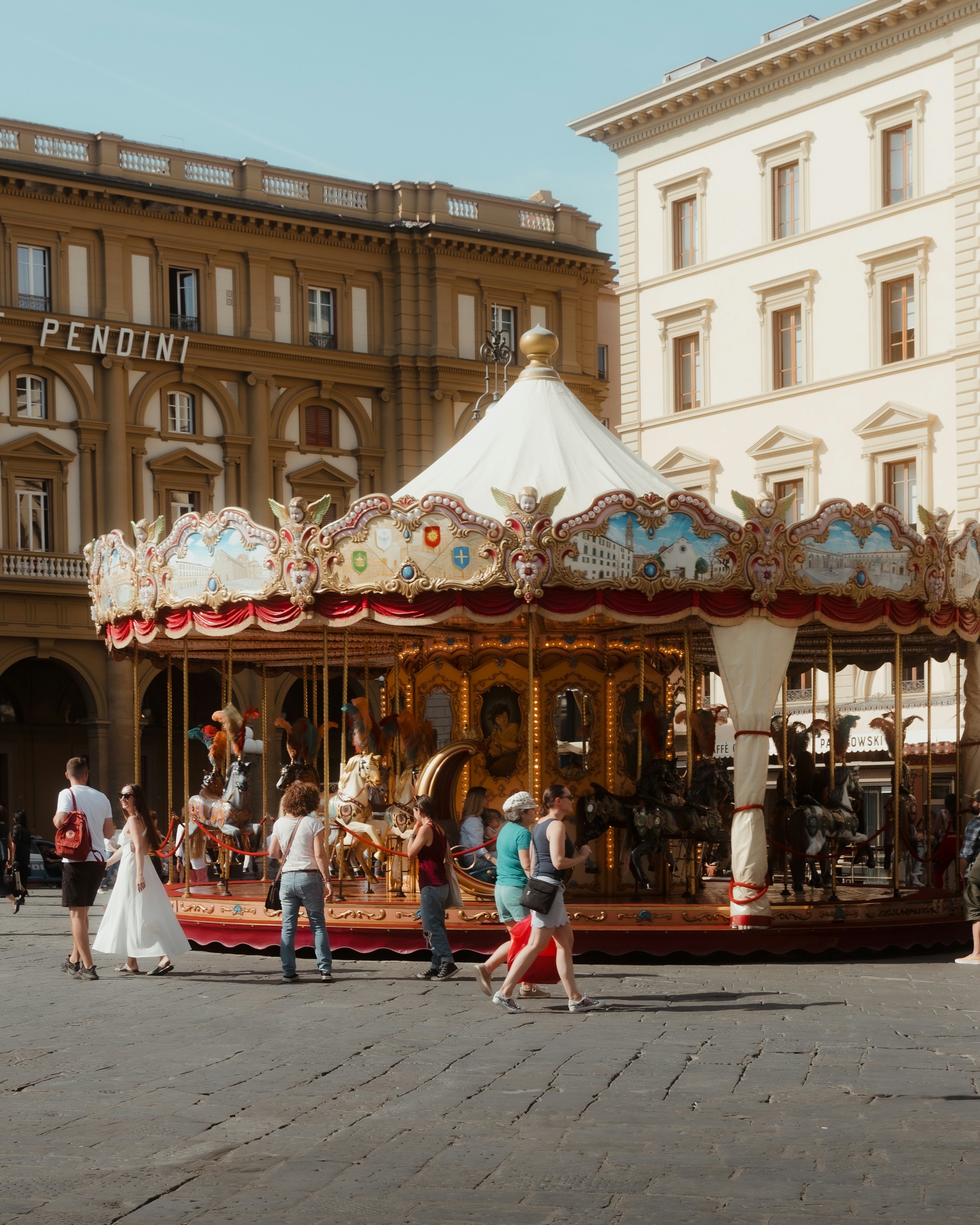 People walk in front of an old-fashioned horse-drawn carousel